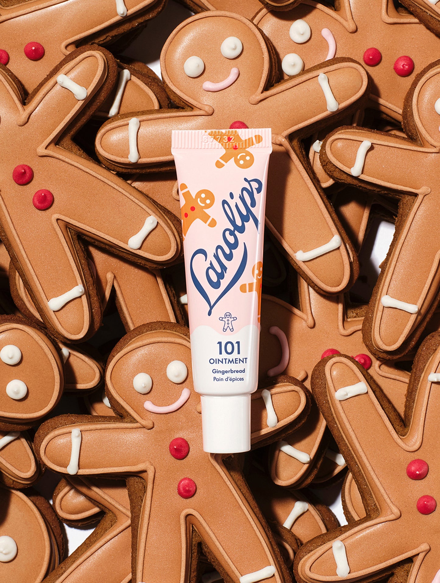 A tube of Lanolips 101 Ointment Multi-Balm Gingerbread surrounded by gingerbread cookies. Embrace warm spice and soft lips with this limited edition festive gourmand flavour.