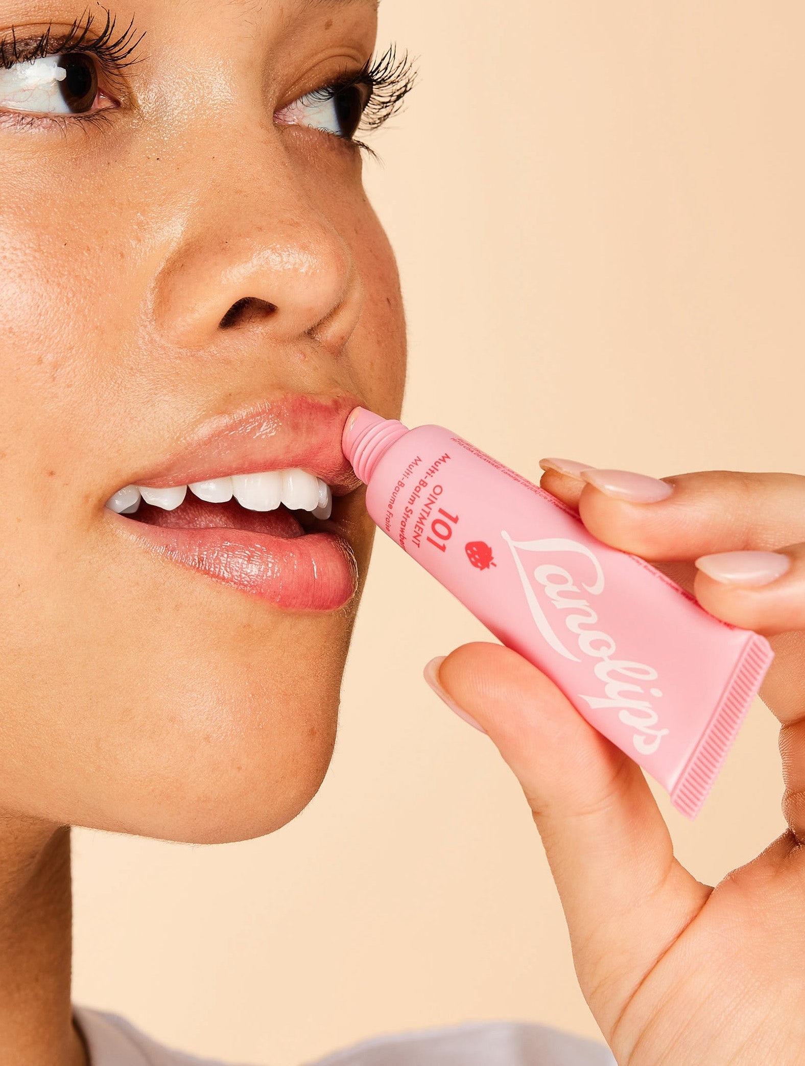 Model applying Lanolips 101 Ointment Multi-Balm in Strawberry to lips, infused with real strawberry extract and vitamin E for sweet, natural hydration. A fruity twist on the iconic Lanolips Original 101 Ointment.