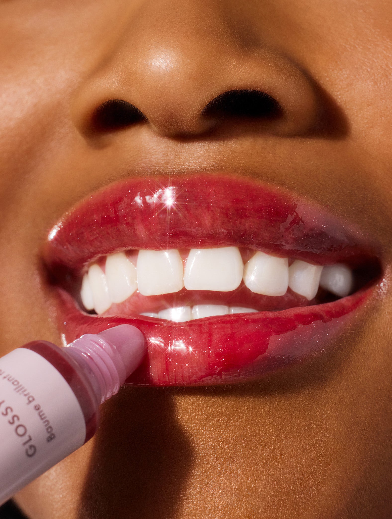 Close up image of a model applying lanolips glossy balms berry lip balm to her lips.