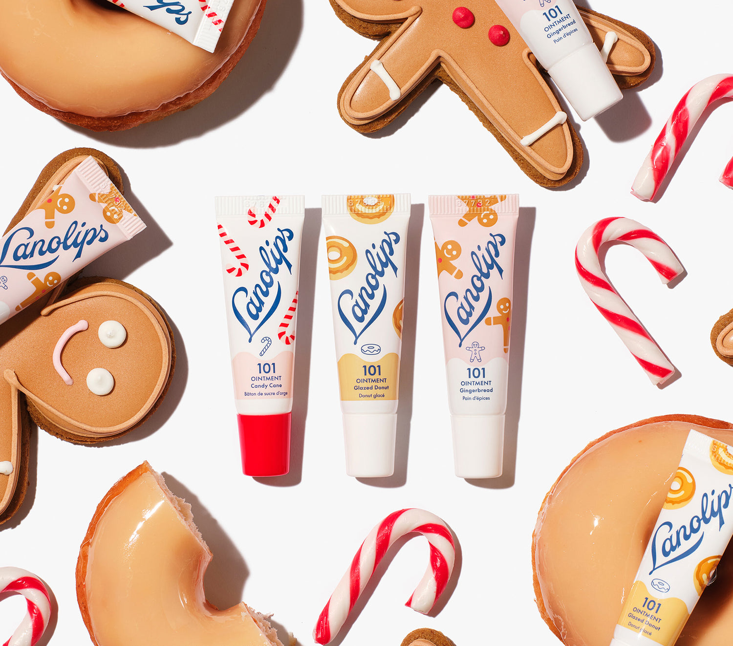 Lanolips 101 Ointment Holiday Mini Bites lip balm trio in Candy Cane, Gingerbread and Glazed Donut flavours, packed with rich lanolin, vitamin E and natural flavours, styled with gingerbread cookies, donuts and candy canes for a holiday twist.