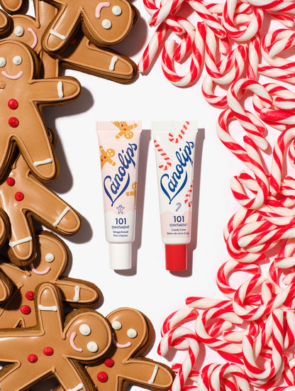 Two tubes of Lanolips 101 Ointment Multi-Balm in Gingerbread and Candy Cane, styled with gingerbread cookies and candy canes on a white background.