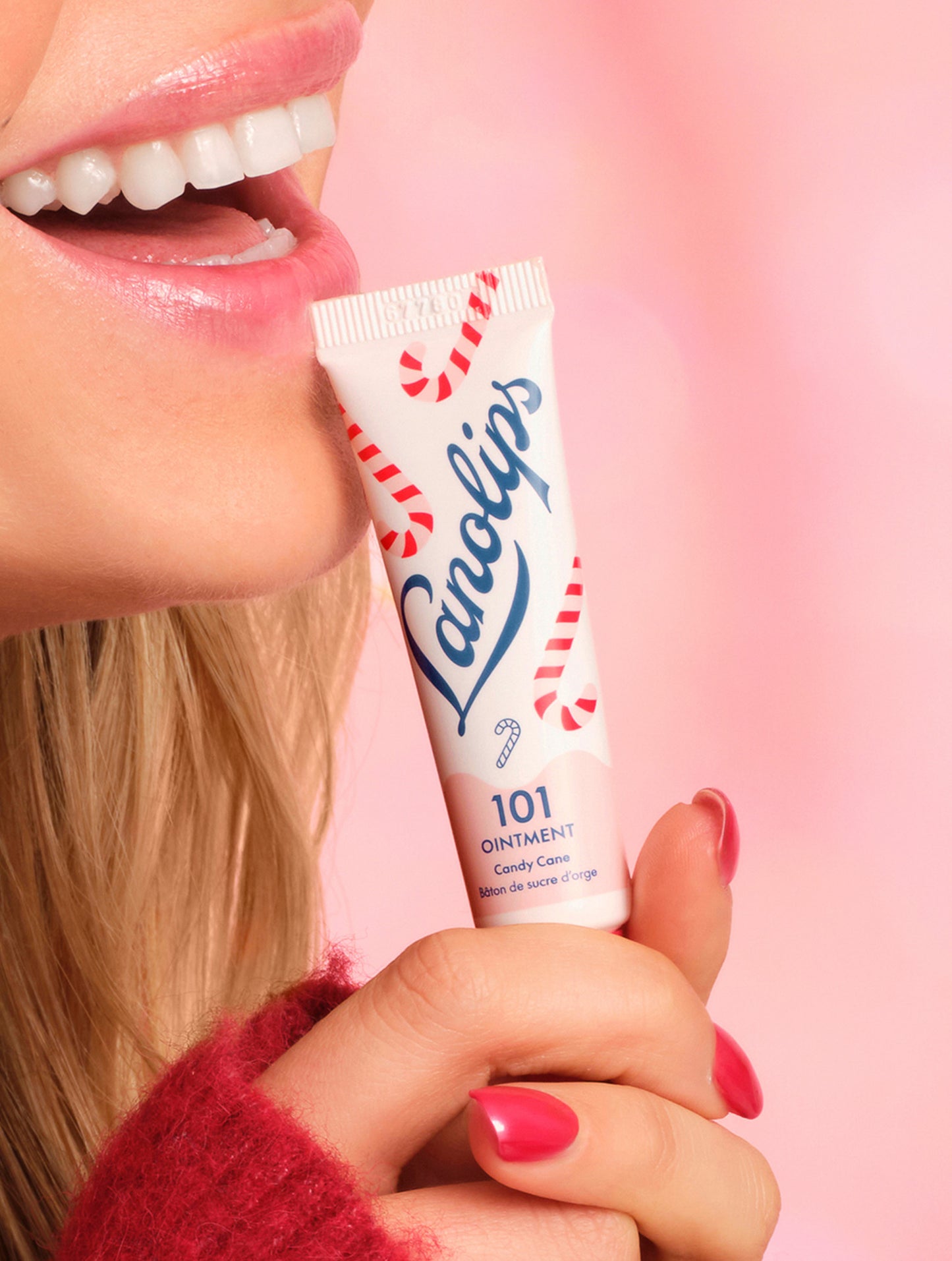 Model holding a Lanolips 101 Ointment Multi-Balm Candy Cane lip balm tube with a pink background.