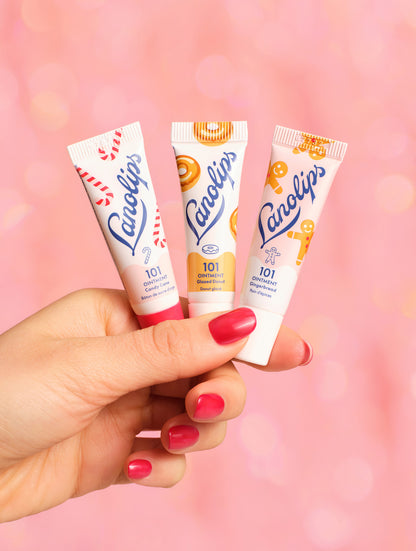 Model holding the trio from the Lanolips Holiday Mini Bites set. The set contains the two new festive flavours - gingerbread and candy cane, as well as a fan-favourite, glazed donut. Packed with rich lanolin, vitamin E, and gourmand flavour, this holiday trio delivers deep hydration for lips, cuticles, dry patches & more.